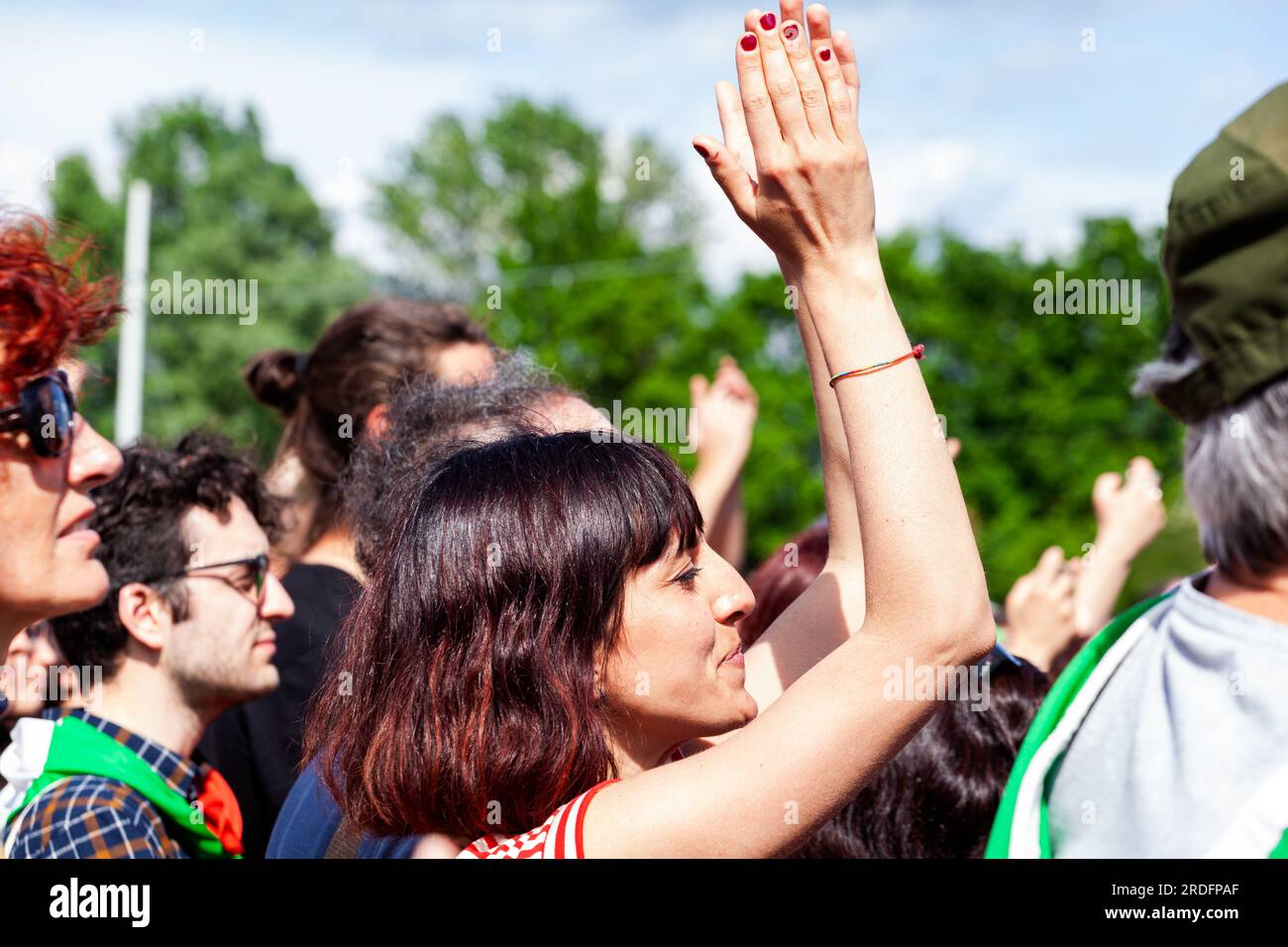 Gattatico, Reggio Emilia, Italy - April 25, 2023: Side view of Young woman clapping hands watching concert in the park at open air Stock Photo
