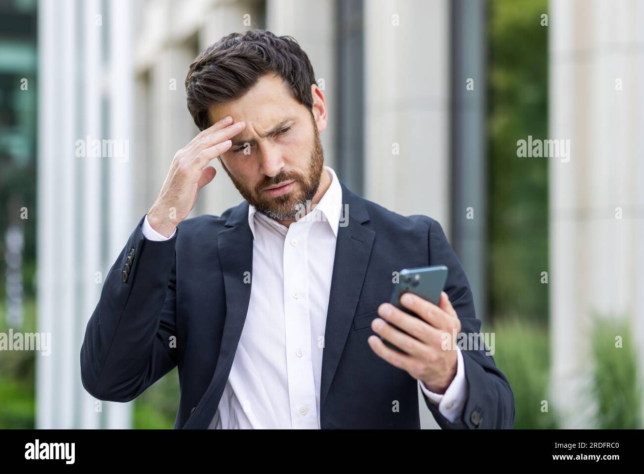 Upset sad businessman reading bad news online using app on phone, thinking man outside office building disappointed with achievement results at workplace, boss depressed. Stock Photo