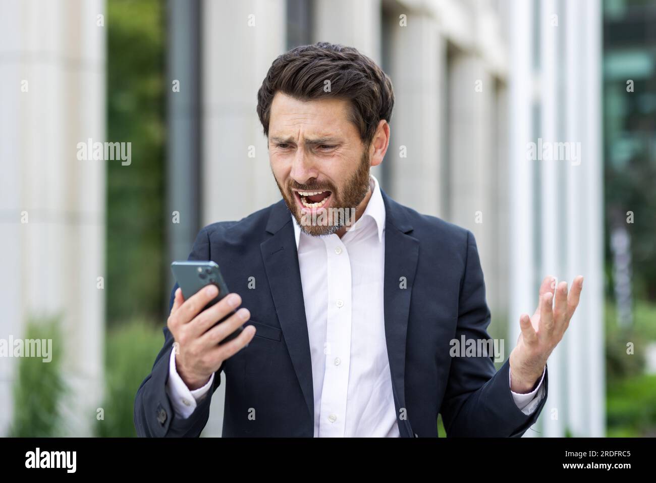 Upset sad businessman reading bad news online using app on phone, thinking man outside office building disappointed with achievement results at workplace, boss depressed. Stock Photo