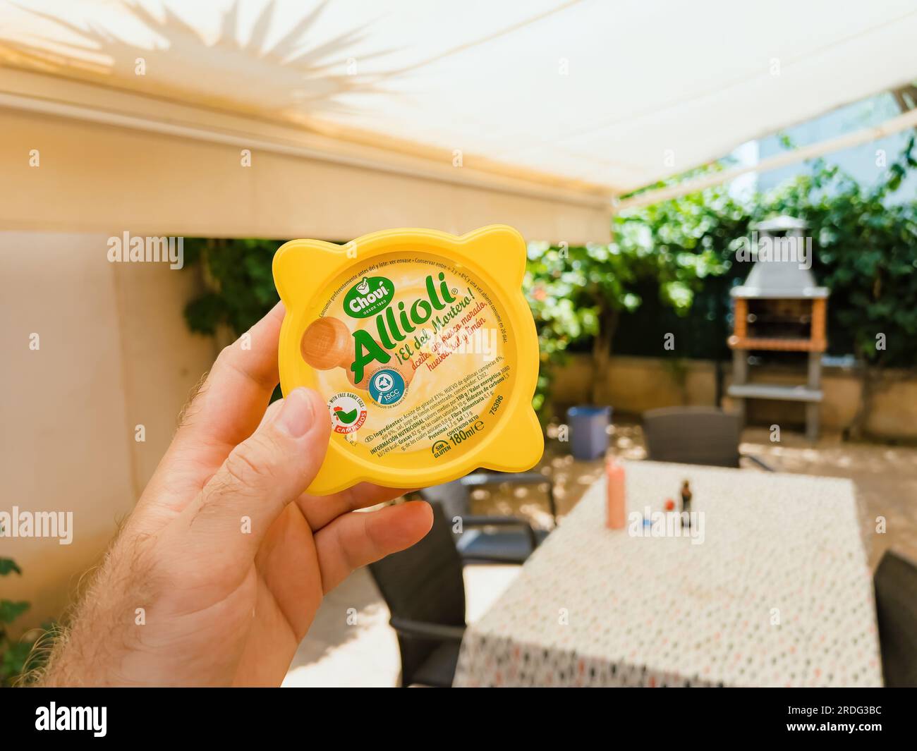 Mallorca, Spain - Jun 30, 2023: A hand holding Chovi brand aioli sauce in yellow plastick package on an outdoor terrace table. Mediterranean flavors in a kitchen setting. Stock Photo