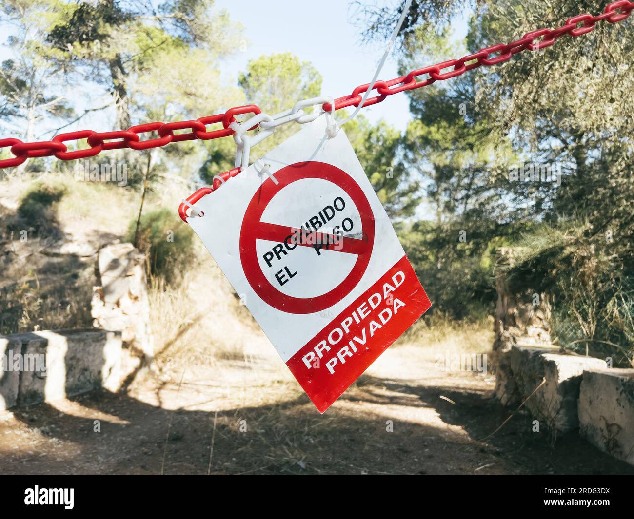 Red warning sign hangs on tree, barring access to private property in spanish language - translated as No trespassing, private property. Ideal for safety communication projects. Stock Photo