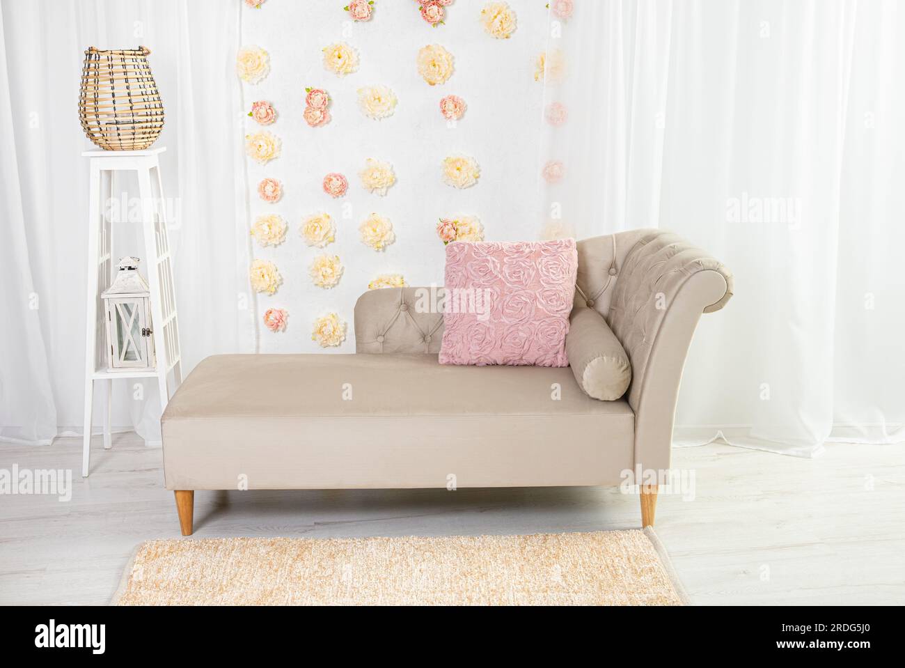 Beige vintage but modern canape style sofa with pink pillow and 3D peony flowers for wall decoration in white interior. Stock Photo