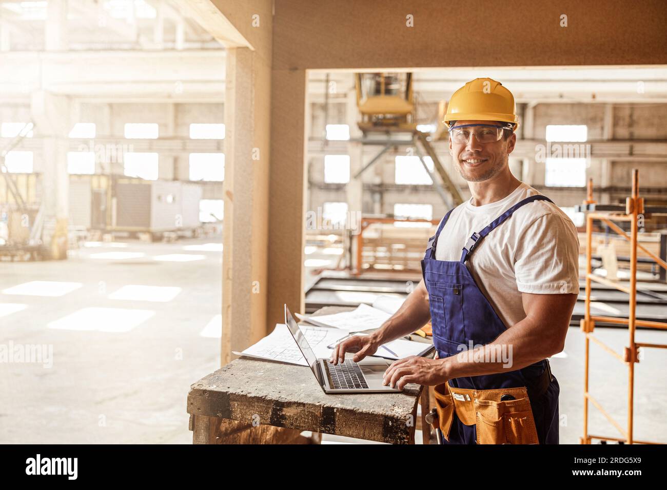 Cheerful male builder using laptop at construction site Stock Photo