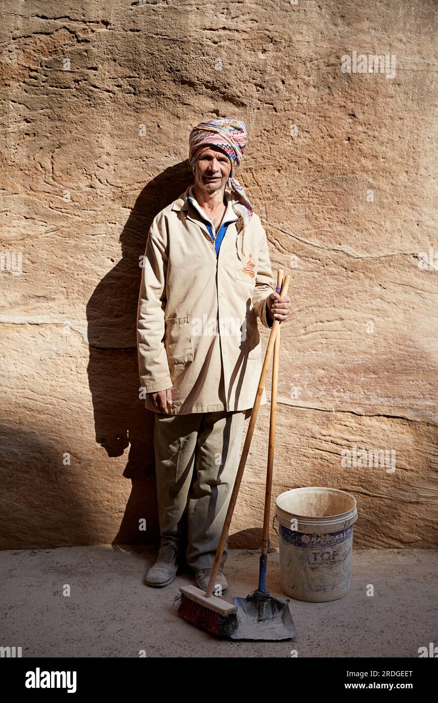 Portrait of cleaner with a broom stood in sunlight by rock face, Petra, Ma'an Governorate, Jordan Stock Photo