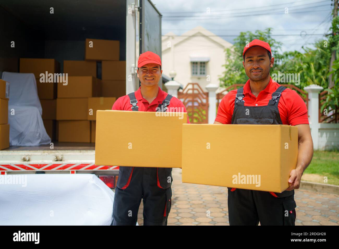 The House Removals company employees stand proudly behind the truck, boxes in hand, wearing smiles that reflect their commitment to a successful move. Stock Photo