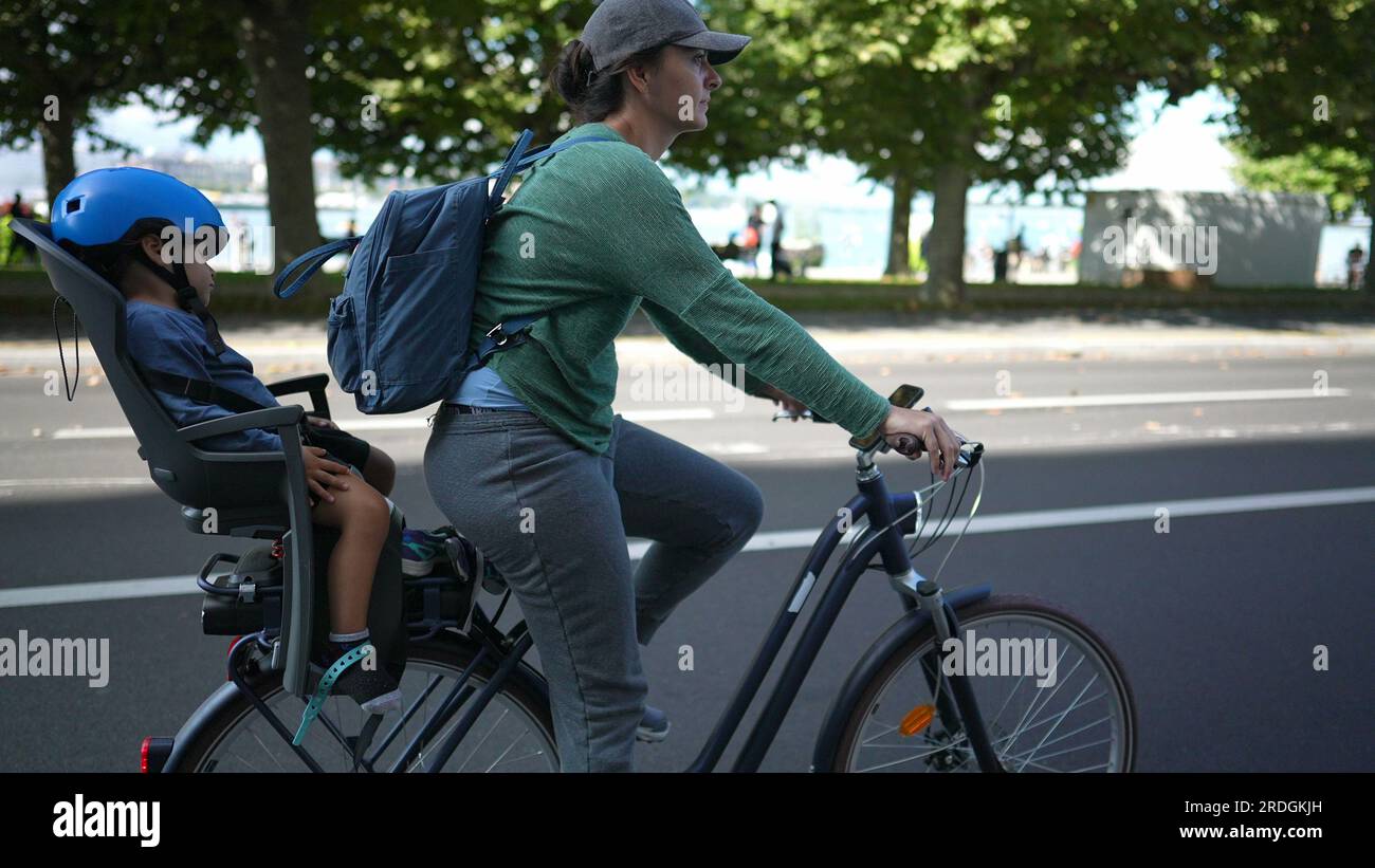 Mother riding bicycle in urban street with child in back seat asleep
