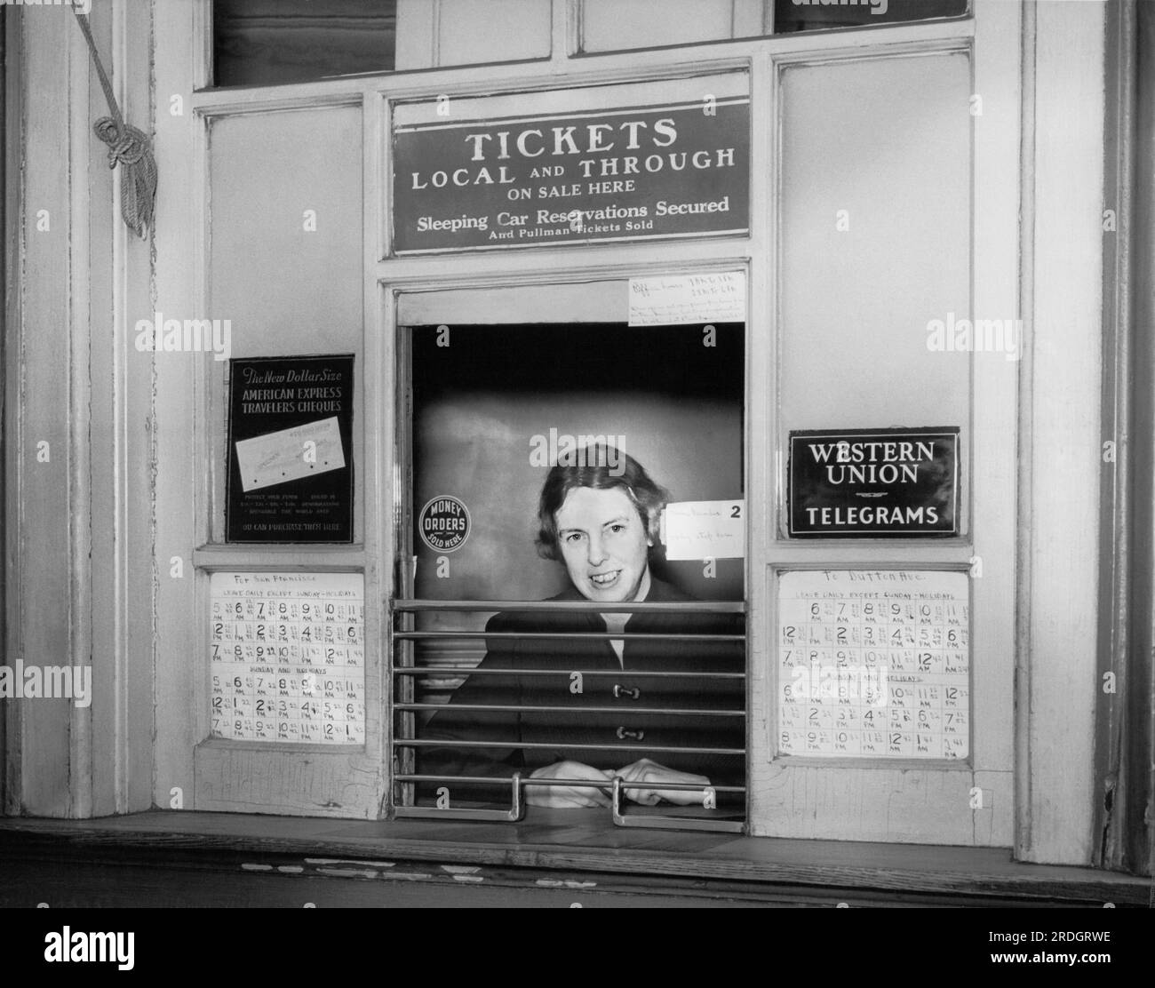 Oakland, California:  c. 1946 A woman at at a railroad ticket counter selling tickets to San Francisco and Dutton Avenue in San Leandro, along with American Express Traveler's Cheques and Western Union telegrams. Stock Photo