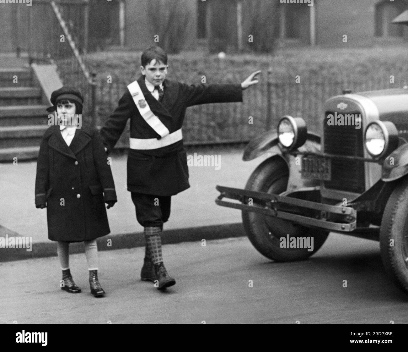 Washington, D.C.:  c. 1928 A schoolboy crossing gusrd stops traffic to let a young girl student cross the street. Stock Photo