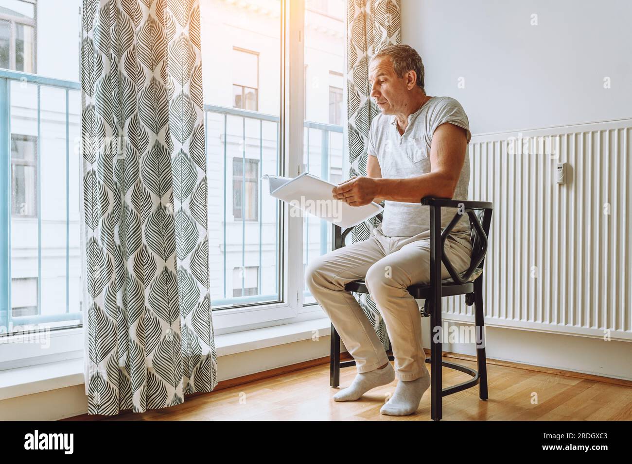 man sitting at window reading folder with documents Stock Photo
