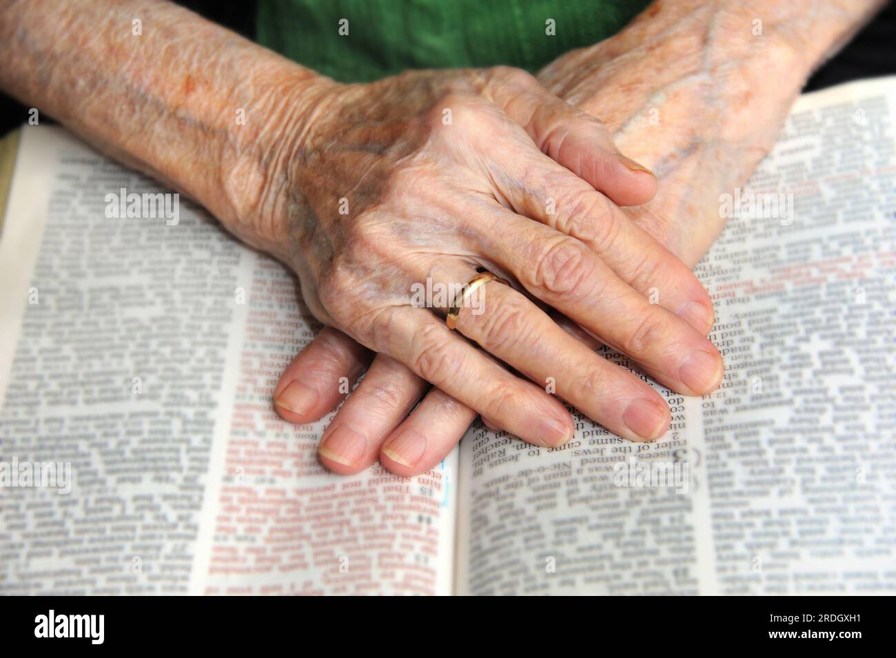 Old hands clasp together over an open Bible.  Hands are wrinkled and worn with the cares of the world. Stock Photo