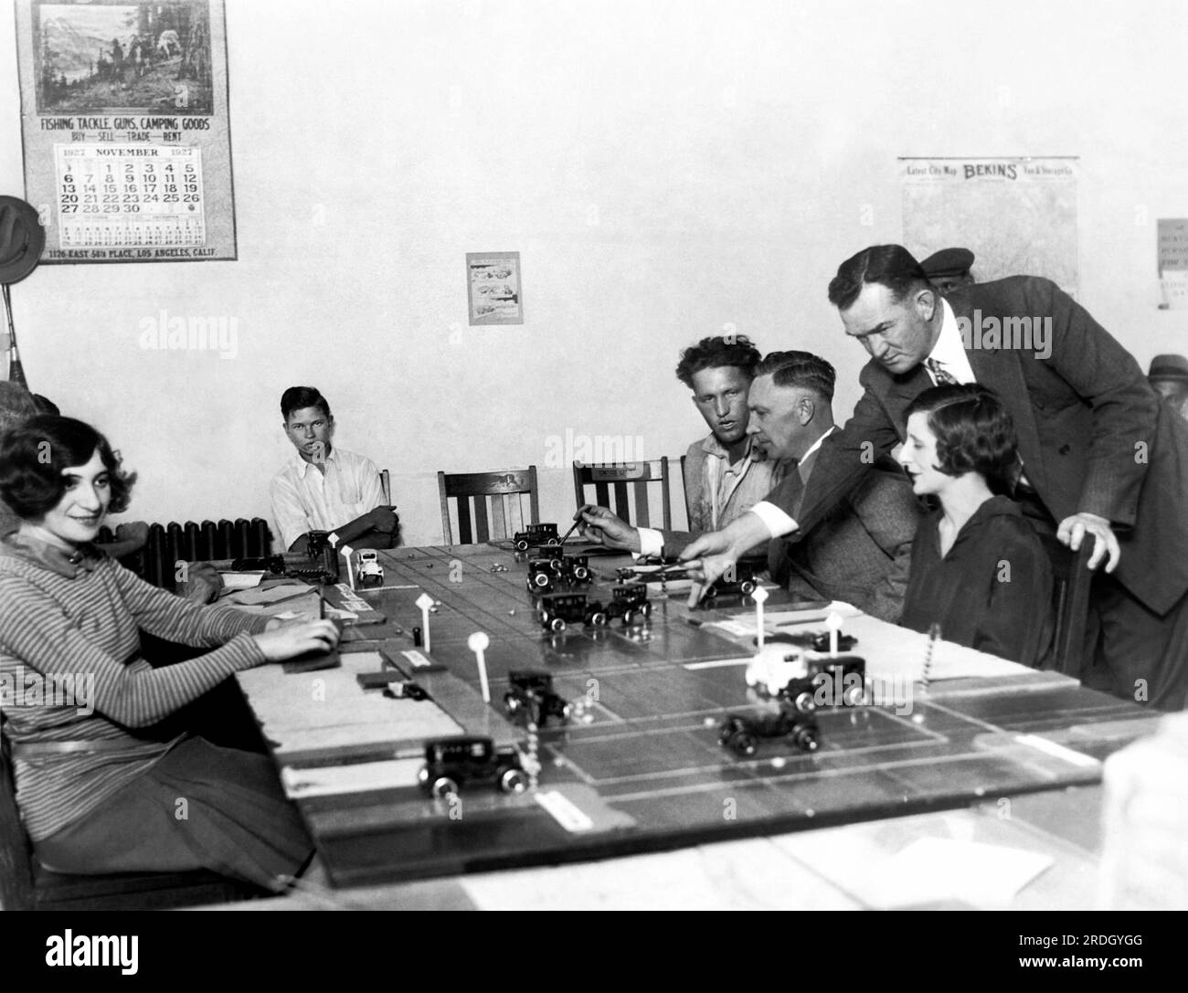 Los Angeles, California:  November 21, 1927 Drivers' license applicants in Los Angeles first have to demonstrate their knowledge of trafic using model cars on a table with a miniature scene of traffic on a street. Here the examiner is untangling a trsffic jam and expalining to the prospective drivers how it occured. Stock Photo