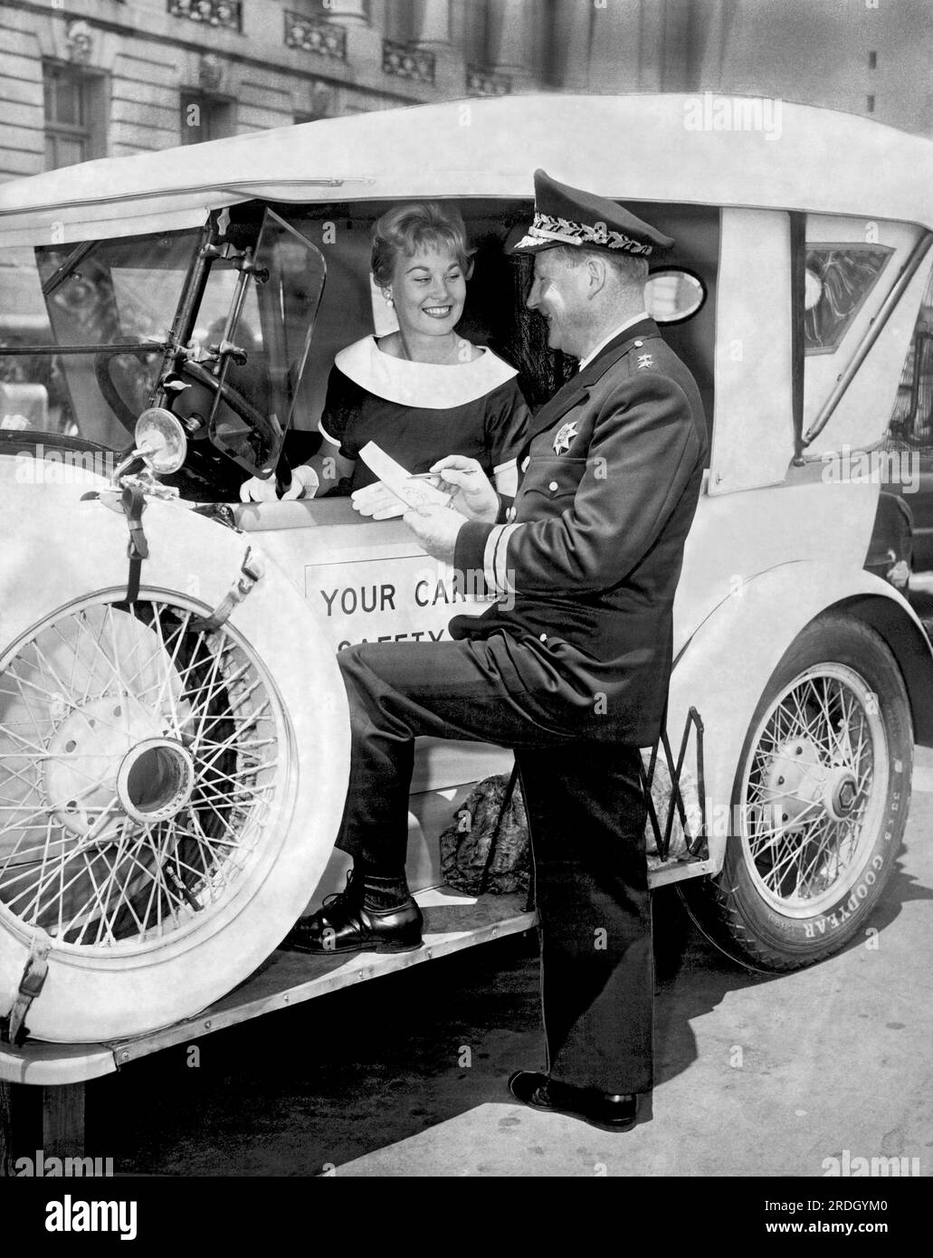 San Francisco, California:  May, 1960 San Francisco Chief of Police Tom Cahill performing a safety check on an old car with a pretty driver. Stock Photo