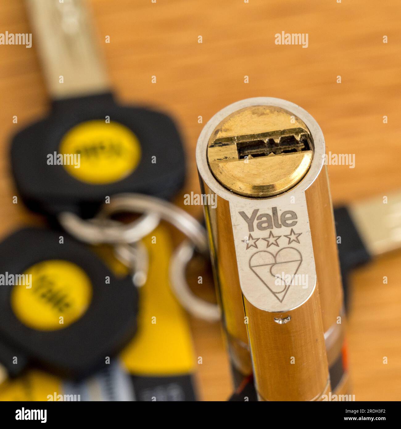 High security Yale Euro profile cylinder lock with 3 star BS kite mark and brass finish with a set of 3 keys on wooden tabletop. Stock Photo