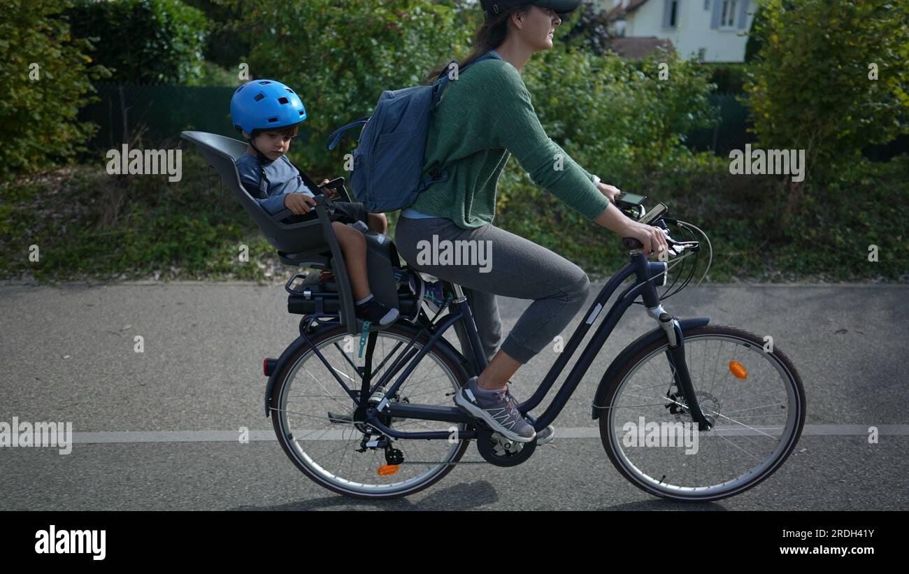mother-riding-bicycle-with-child-in-back-seat-outside-in-urban-green