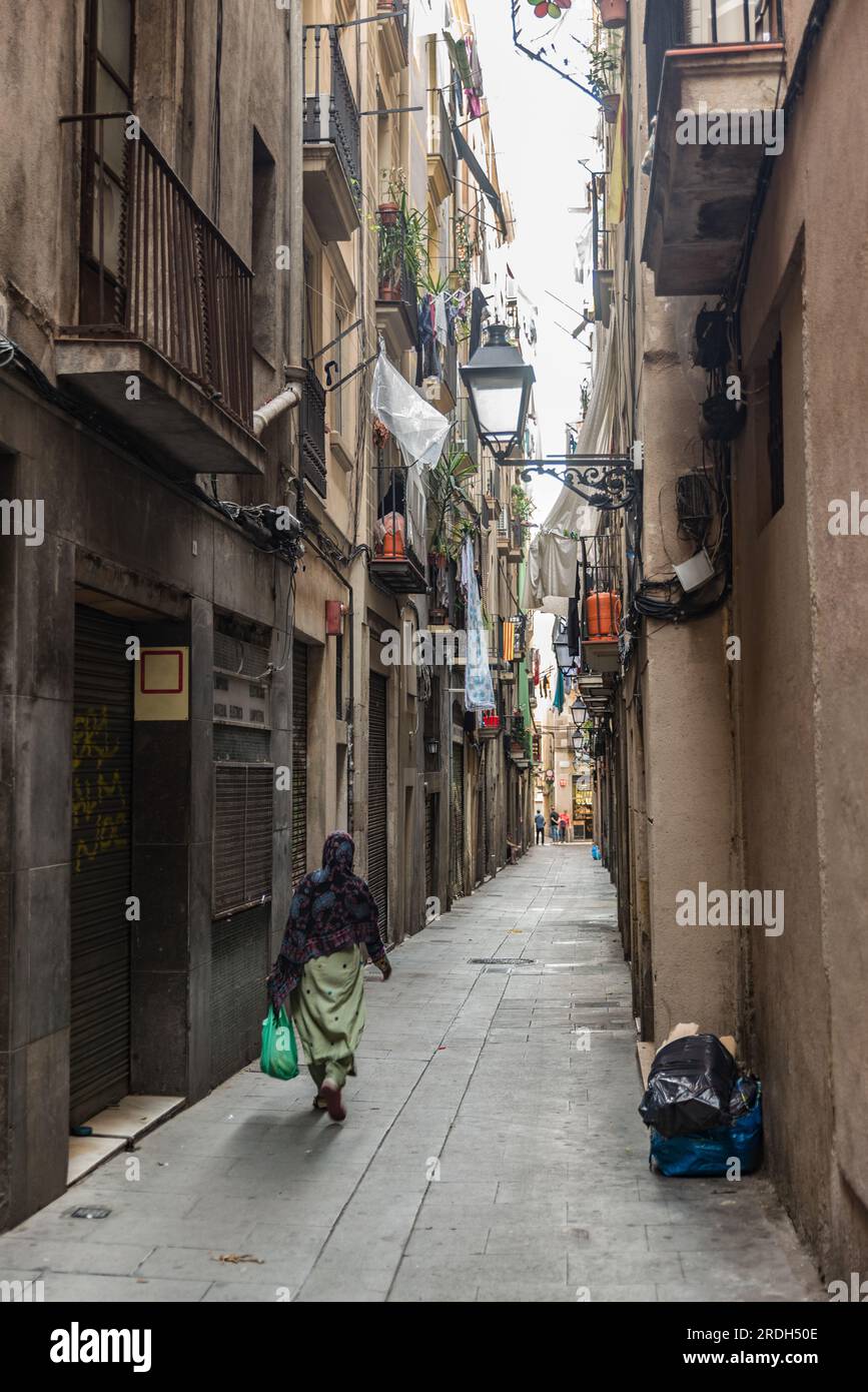 Barcelona, Spain - October 11th, 2015: Headscarfed woman carrying a groceriesbag strawling through an alleyway. Stock Photo