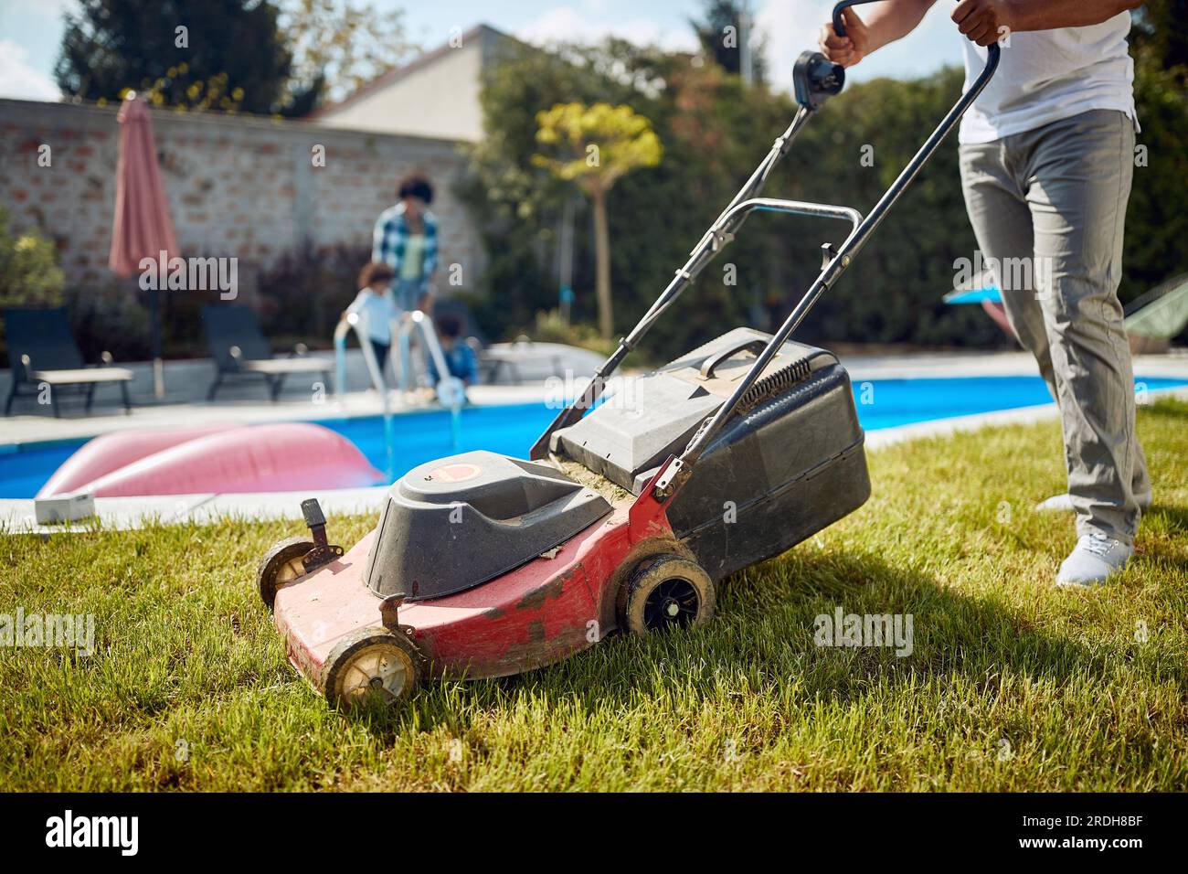Low section shot of young man mowing grass by the pool, clean cut grass. Family weekend in a villa. Stock Photo