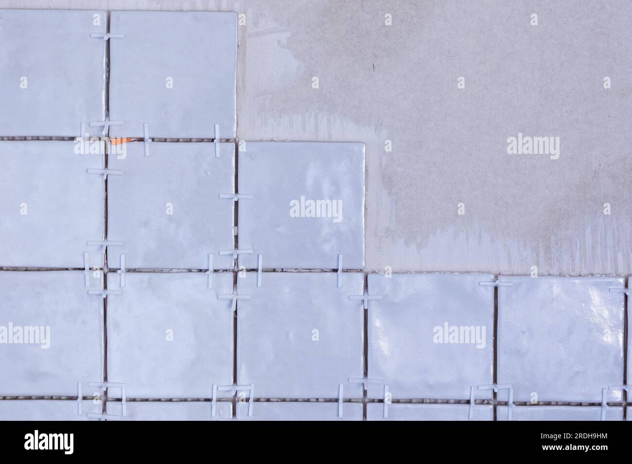 A portrait of an unfinished tile wall, with plastic white joint spacers still in the junctures