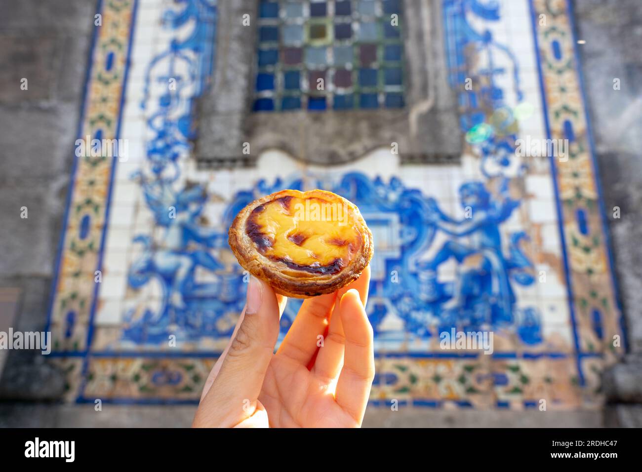 holding Pastel de nata in Porto Portugal in front of beautiful white blue azulejo tiles . Stock Photo