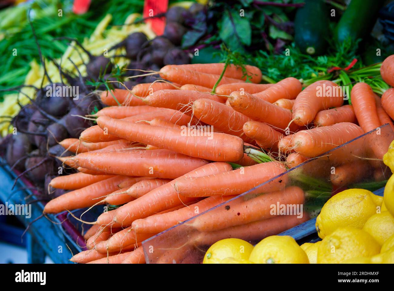 Heap of carrots laying in a market stall in front of other vegetables for sale at farmers market. Stock Photo