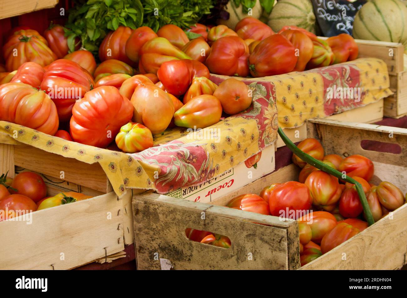 Red beef tomatoes in wooden boxes with fabrics for sale at farmers market in Provence in France. Stock Photo