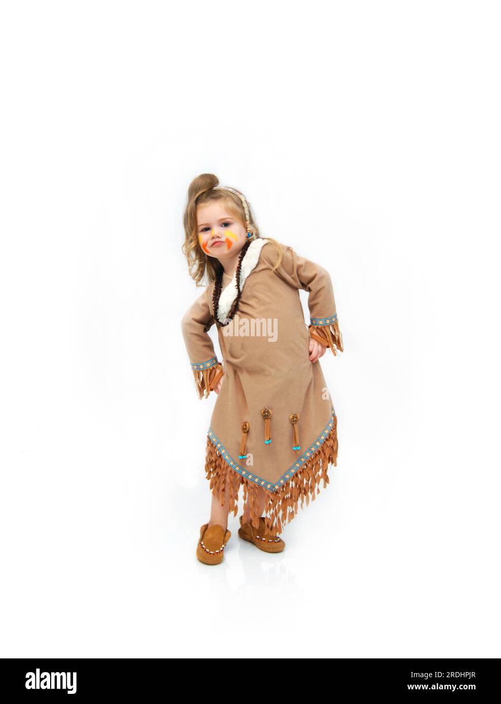 Adorable indian princess wearing fringed leather dress and moccasins, dances a rain dance or war dance.  Her face is comical and her hands are on her Stock Photo