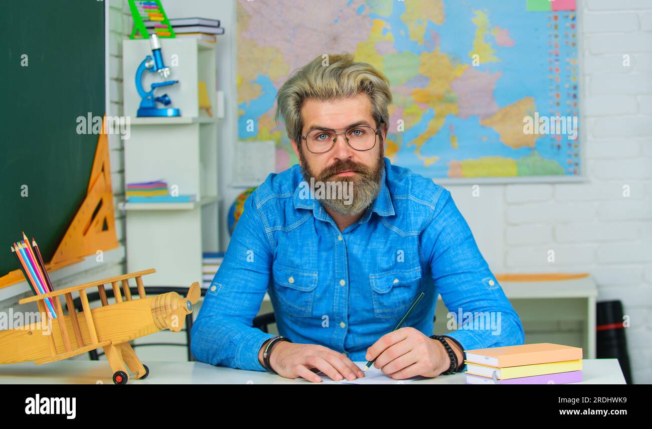 Male student in glasses preparing for test or exam. Student sitting at desk in class at university writing notes in notebook with pencil. Back to Stock Photo