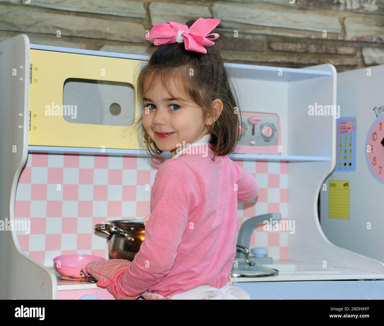 Little girl pretends to be the mom cooking diner for her family. She is ...