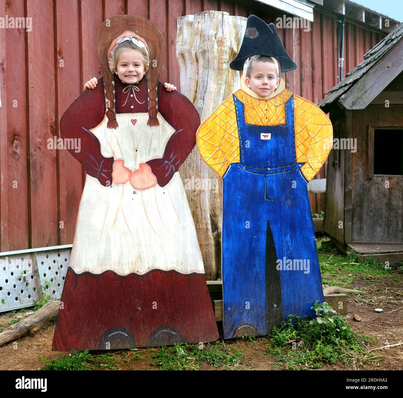 Boy and Girl pretend to be farmers by posing with wooden figures.  They are poking their heads through face holes and smiling.  Both are enjoying harv Stock Photo