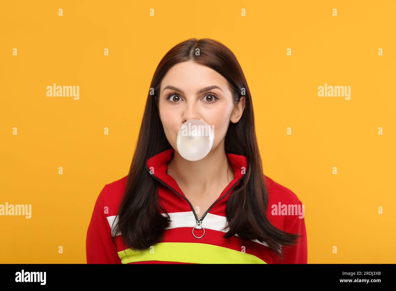 Beautiful woman blowing bubble gum on orange background Stock Photo - Alamy