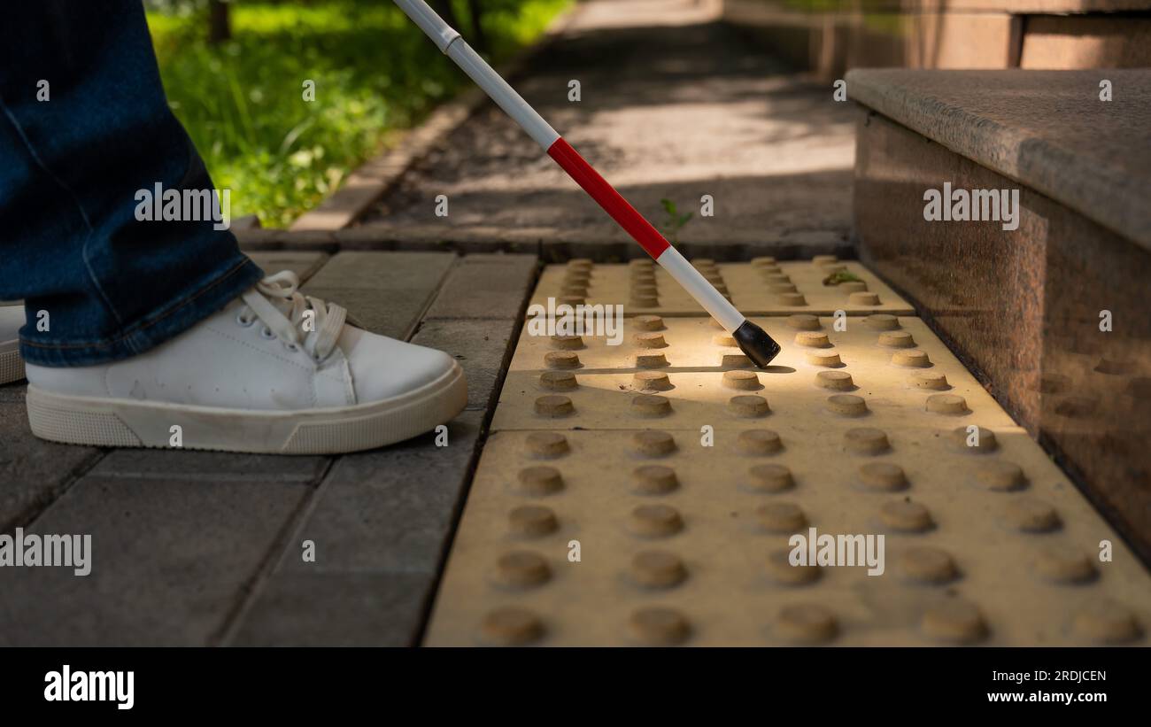 Close-up of female foot, walking stick and tactile tiles. Blind woman climbing stairs using a cane.  Stock Photo