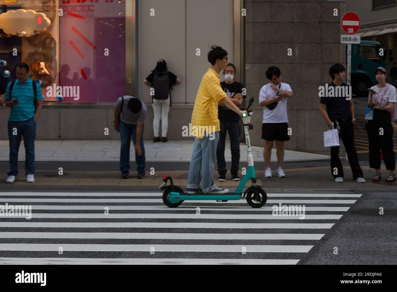 A man rides a Luup e-scooter past a pedestrian crossing in Shinjuku, Tokyo, Japan. Stock Photo