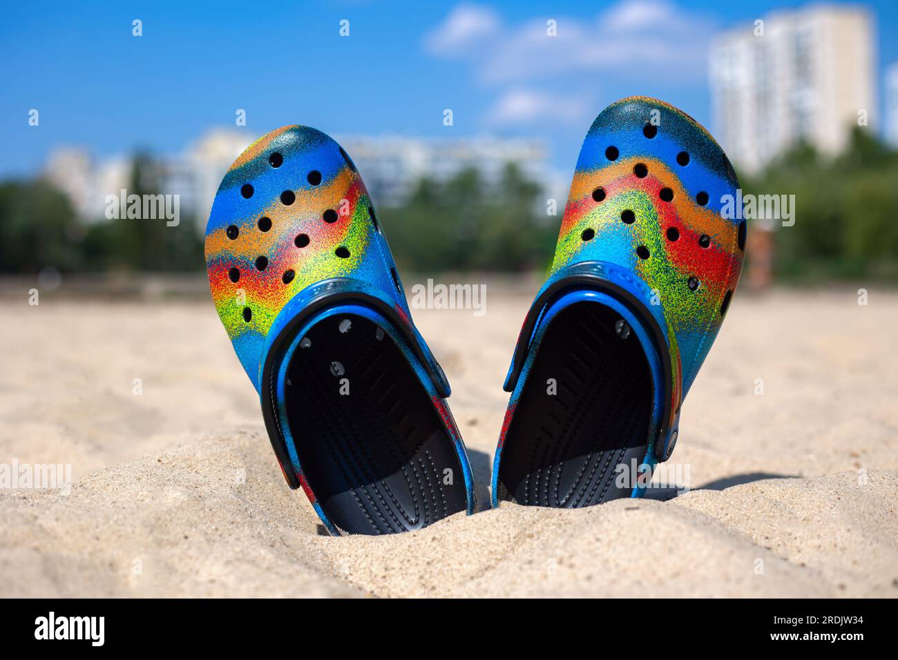 Ukraine Kyiv July 04. 2022 Multi colored Crocs stick out in the sand. The beach and houses are blurred in the background. olorful trendy croc bea Stock Photo Alamy