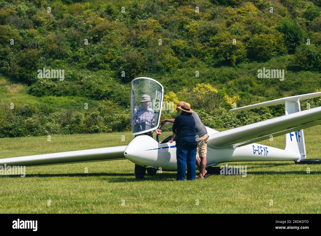 People talking around a glider with the canopy up at an airstrip in