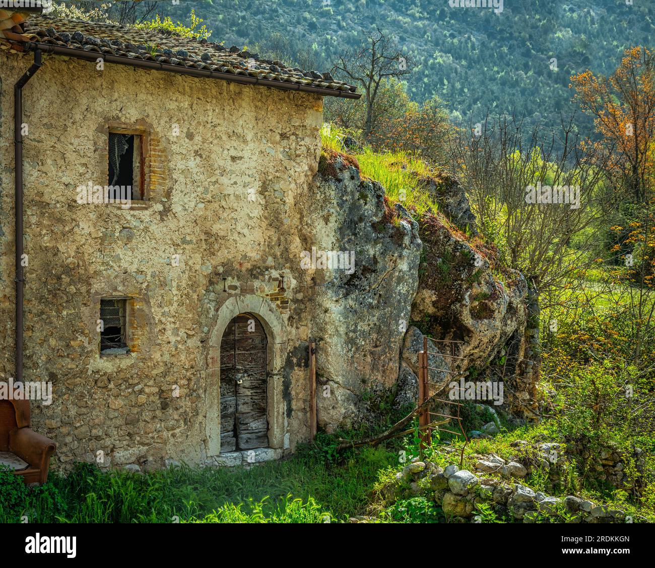 ancient rural stone house leaning against a boulder Stock Photo