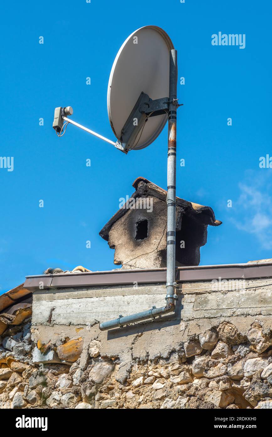 An old smoke-blackened chimney pot and a modern satellite dish for receiving television signals. Contrasts. Pacentro, L'Aquila province, Abruzzo, Ital Stock Photo