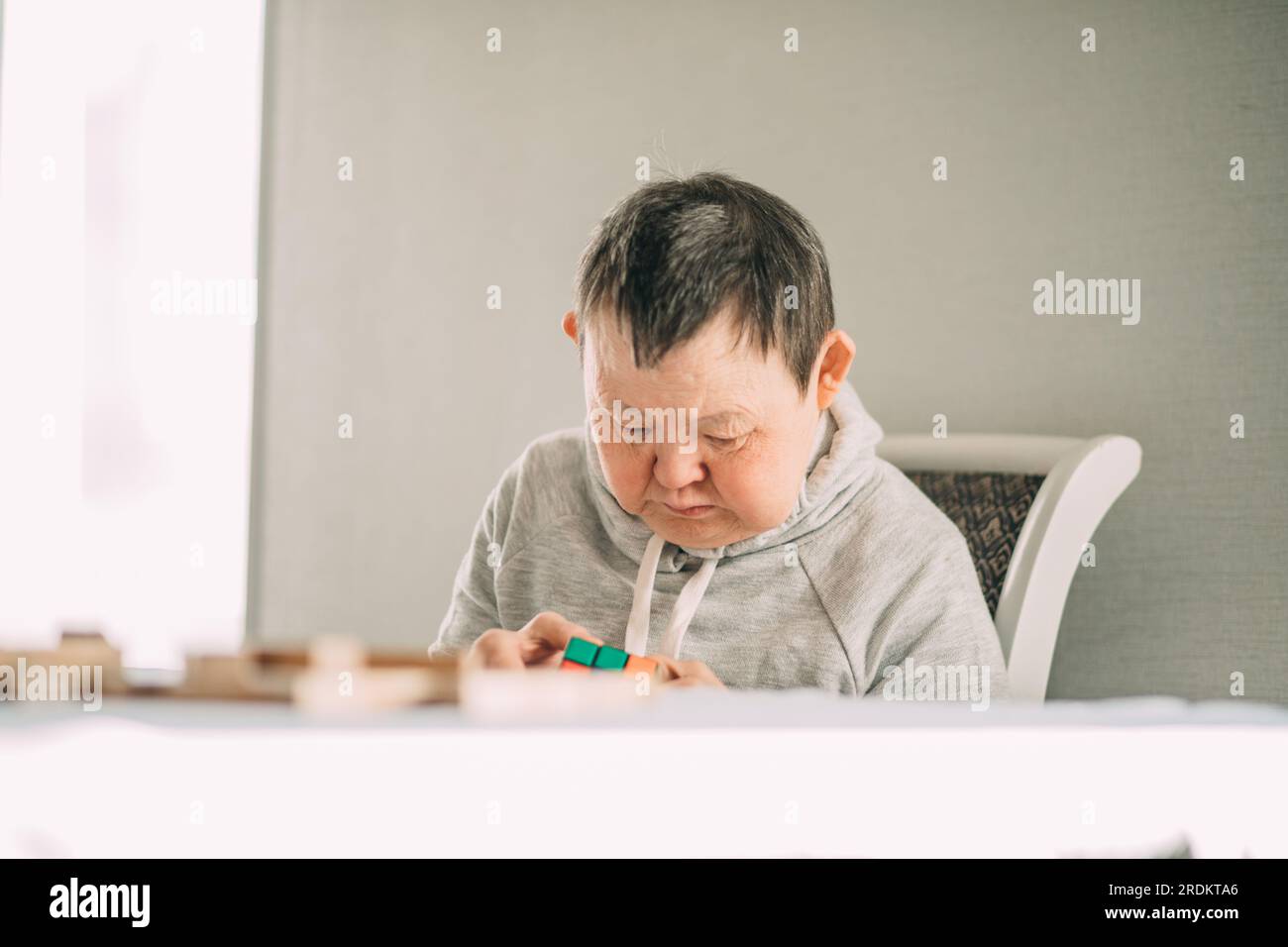 Combining Empathy and Fun: The Extraordinary Story of an Elderly Woman with Down Syndrome Ponders Over Board Games Stock Photo