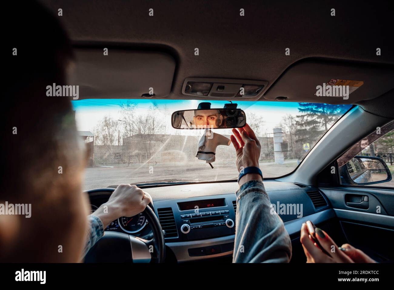 The young adventurer ensures a safe journey by adjusting the car's rearview mirror, covering the topic of travel and exploration Stock Photo