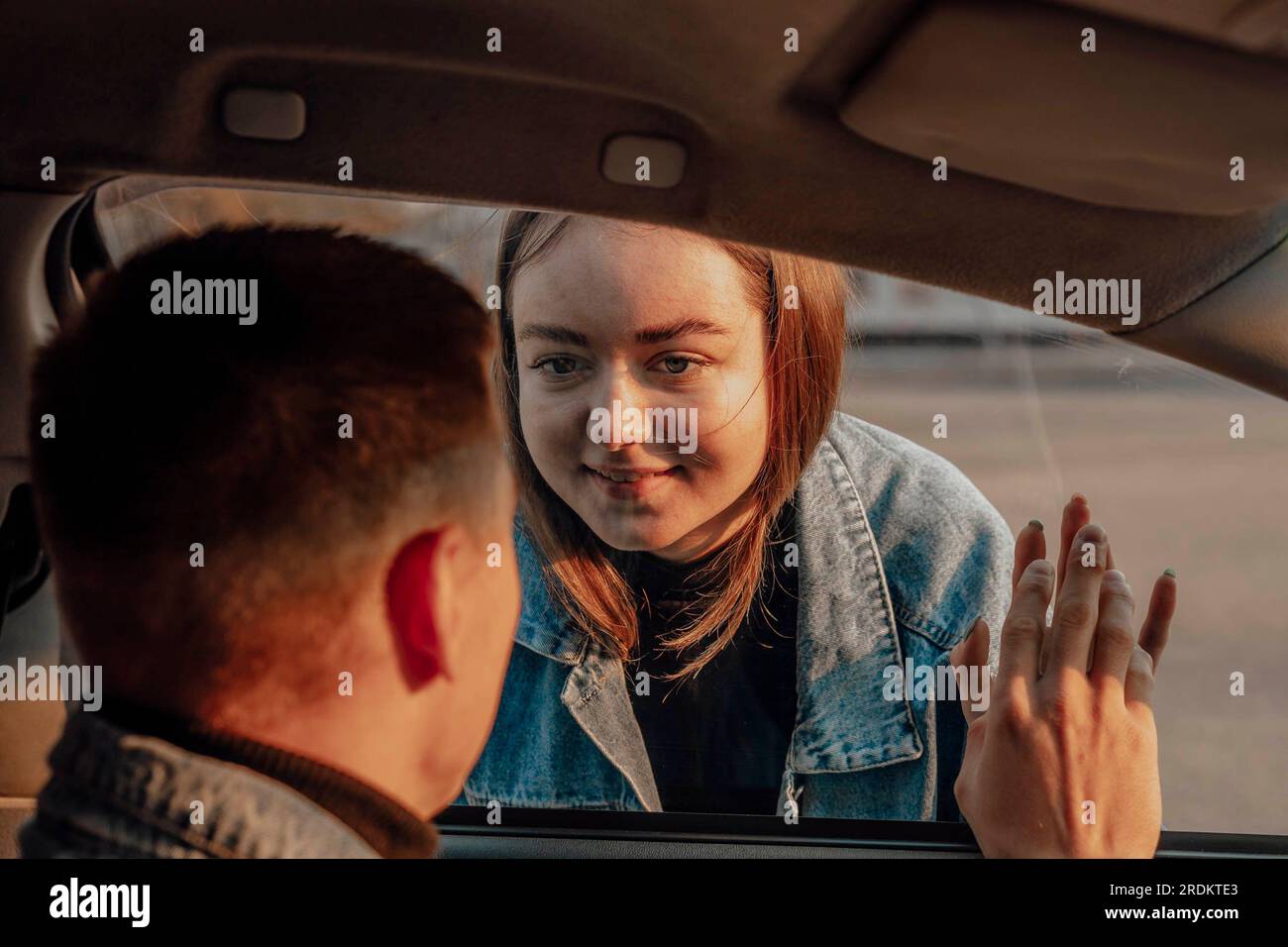 girl saying goodbye to boy through a car window before travel Stock