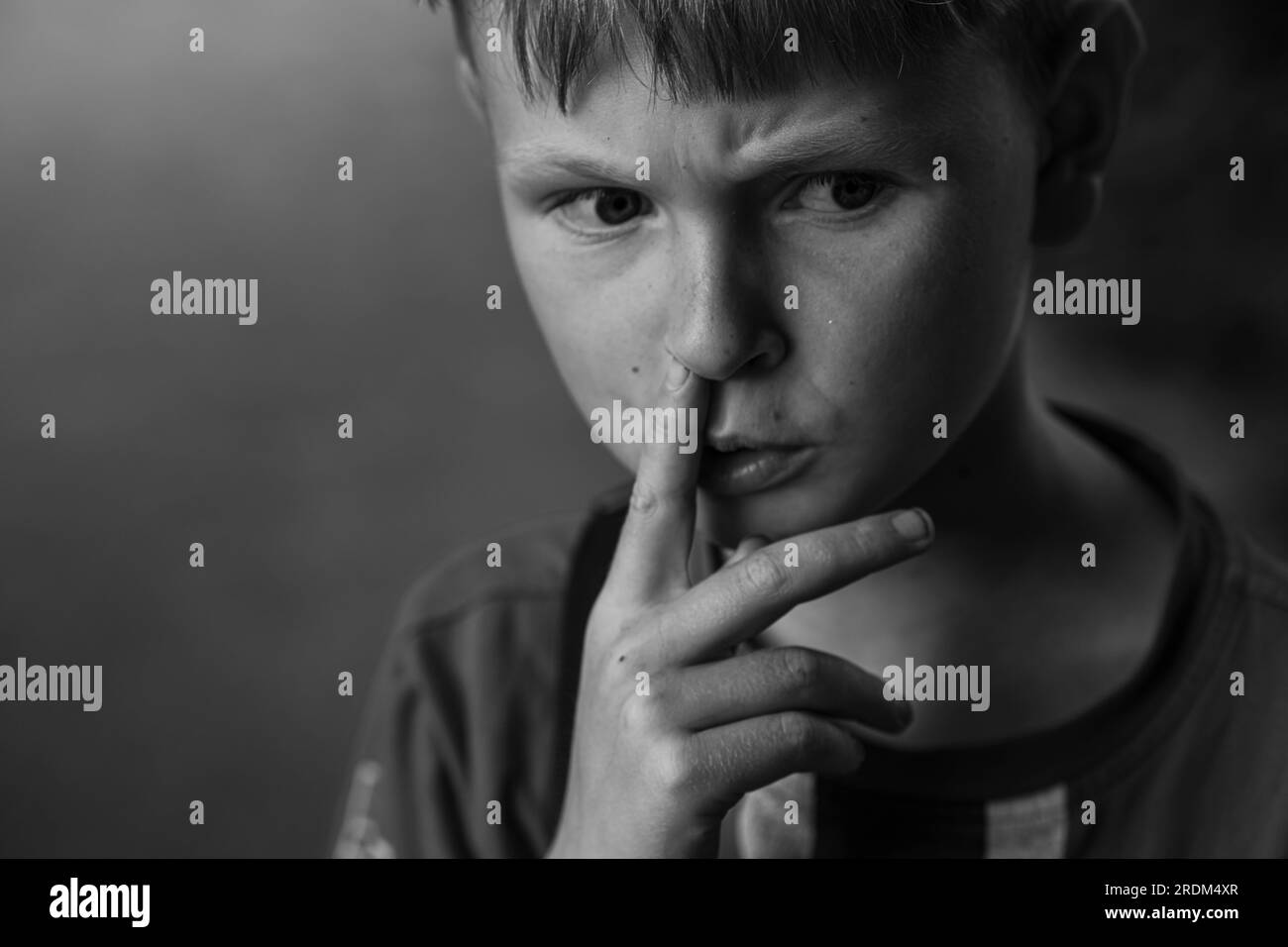 Portrait of a boy picking his nose. Thoughtful boy furrows his brows. Black and white image. Stock Photo