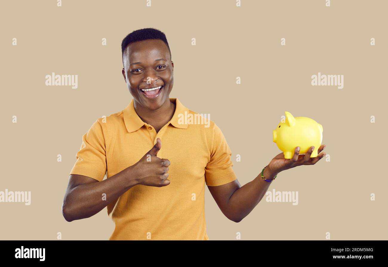 Happy young African American man holding piggy bank, smiling and giving ...