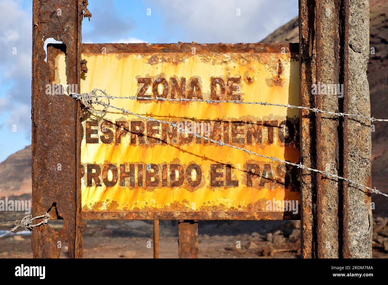 A rusty warning sign in Spanish: zona de desprendimiento prohibido el paso (English: entry prohibited, falling stones zone). Stock Photo