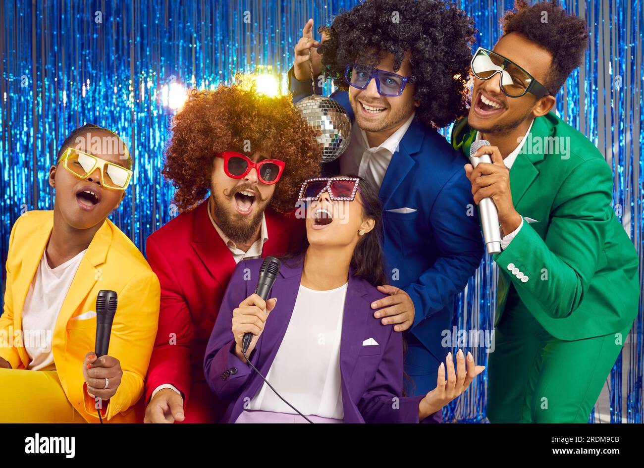 Happy multiracial friends wearing disco style singing karaoke in club party on blue backgrpund. Stock Photo