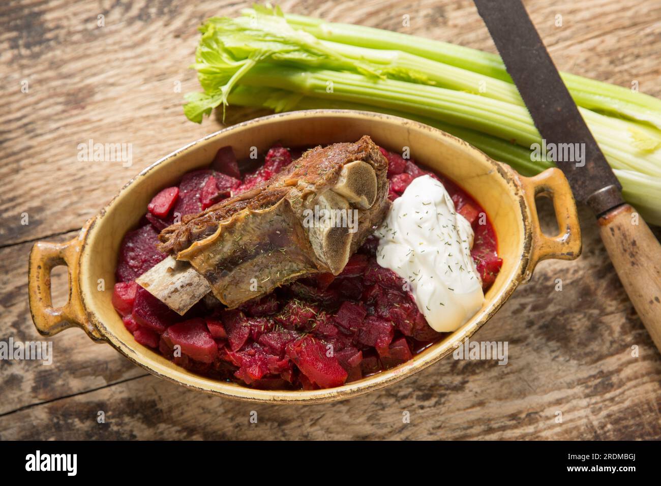 Homemade Borscht soup served with a slow cooked beef rib and a dollop of creme fraiche. Displayed on a wooden chopping board. England UK GB Stock Photo