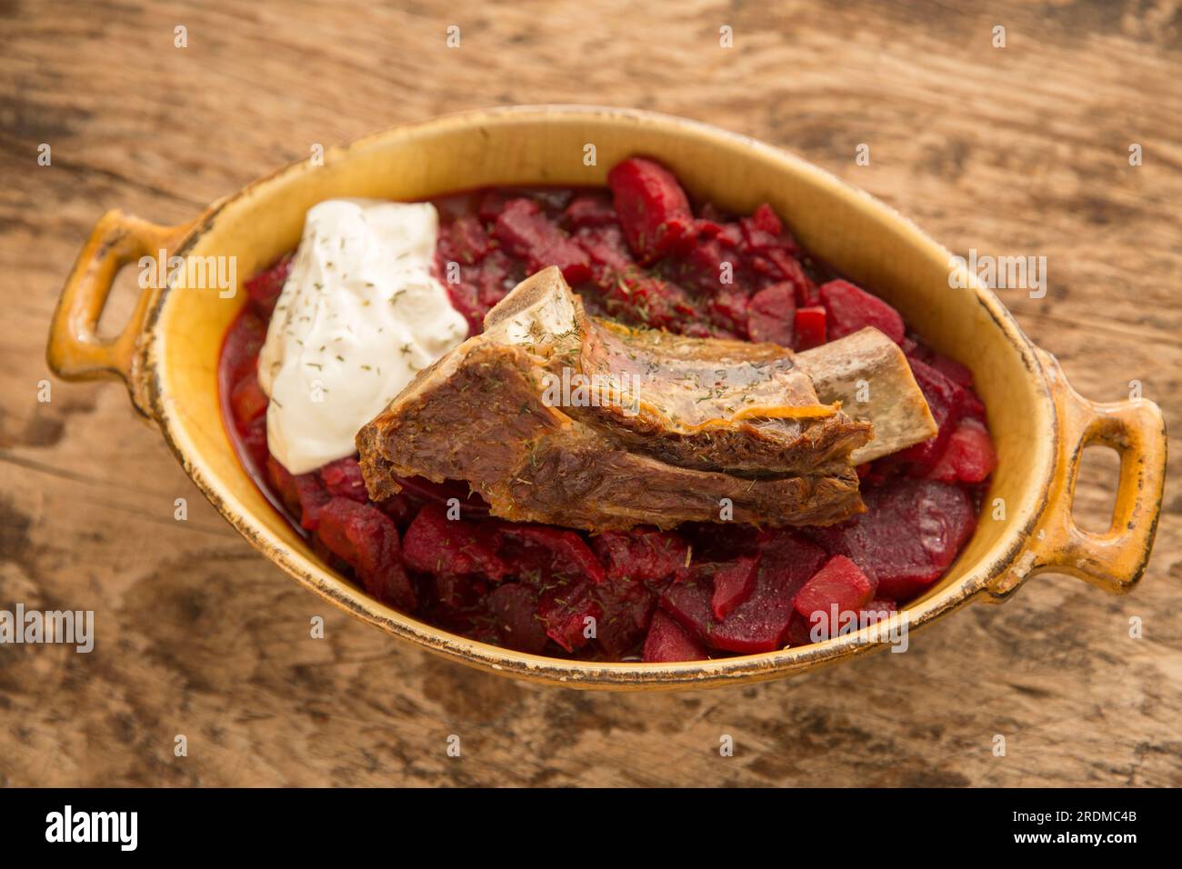 Homemade Borscht soup served with a slow cooked beef rib and a dollop of creme fraiche. Displayed on a wooden chopping board. England UK GB Stock Photo