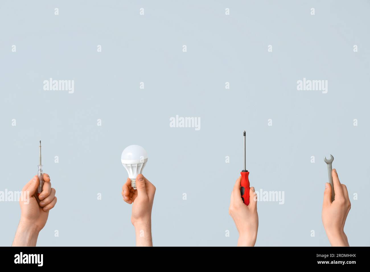 Electrician hands with light bulbs and tools on grey background Stock Photo