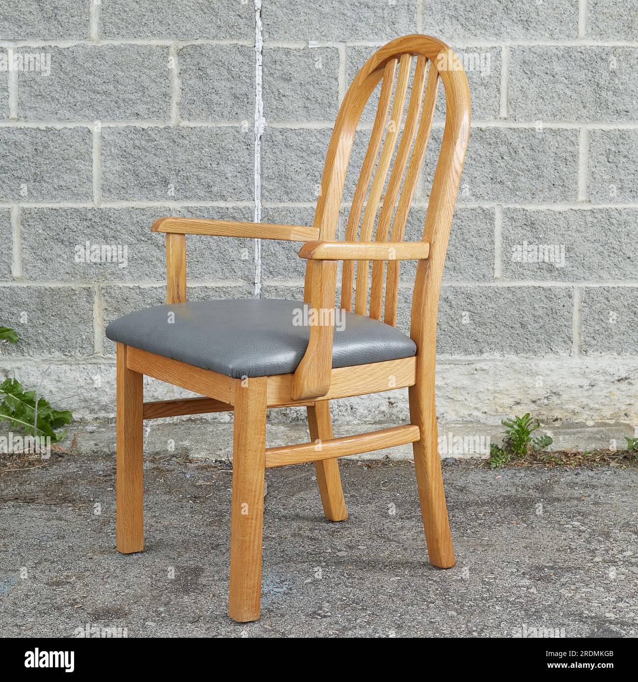 Oak Dining Chairs, single light wood chair with grey leather upholstery. Front view. Photographed against a grey brick background. Stock Photo