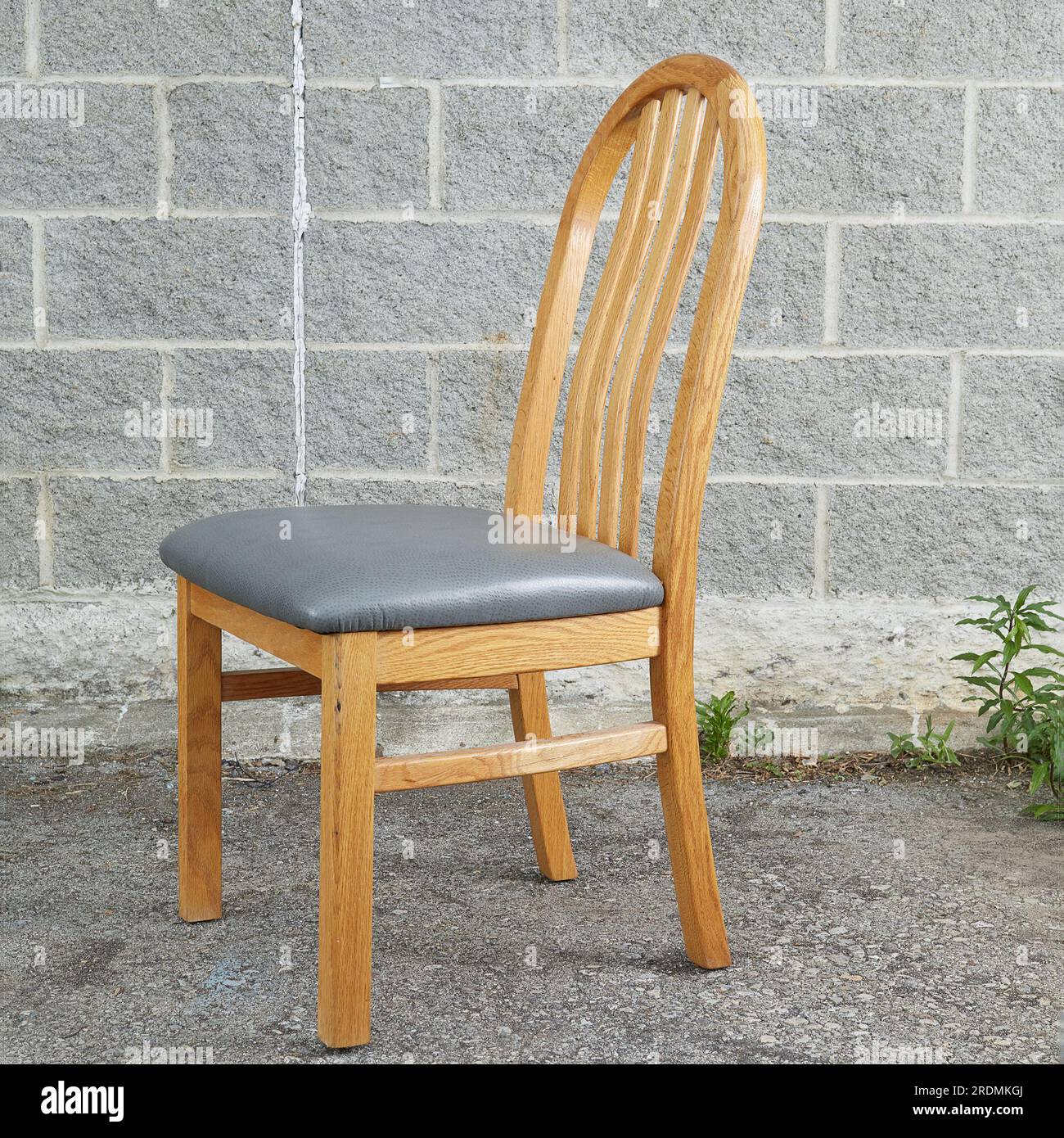 Oak Dining Chairs, single light wood chair with grey leather upholstery. Front view. Photographed against a grey brick background. Stock Photo
