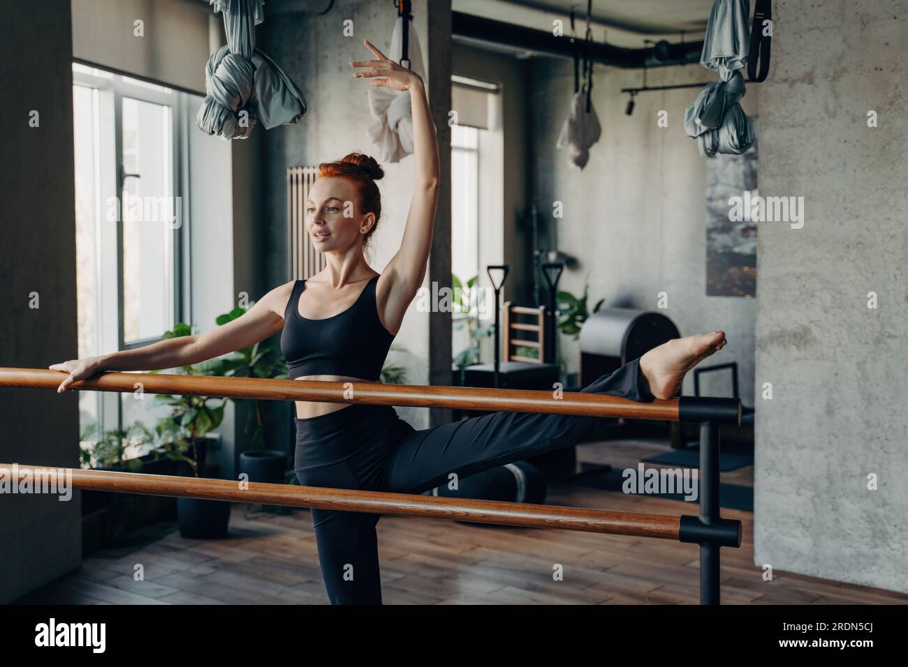 Graceful fit ballerina in black sports bra and leggings stretches with  splits at the ballet barre during a Pilates class in the studio. Embracing  a he Stock Photo - Alamy