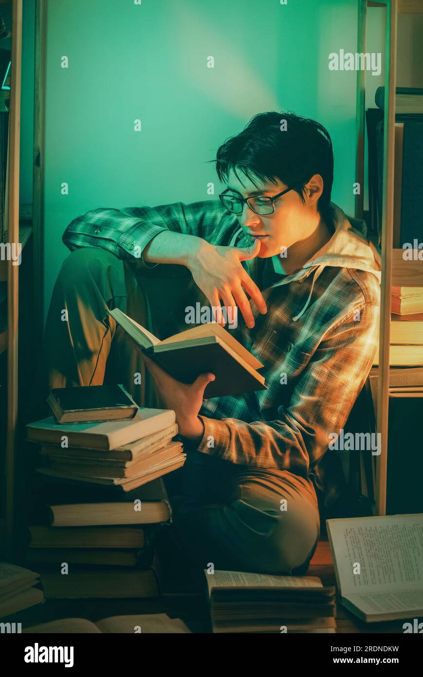 An young, handsome student wearing glasses, sitting amidst stacks of ...