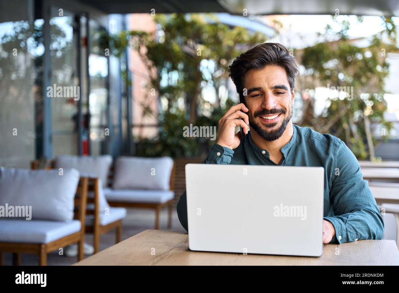 Smiling Latin business man talking on cellphone working on laptop outdoors. Stock Photo